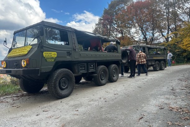 Two military-style 6x6 trucks on a dirt road with people gathered around.