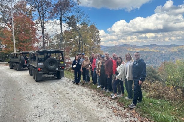 Group of people standing beside two jeeps on a scenic autumn road.