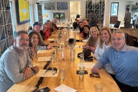 Group of people sitting around a large wooden table in a wine tasting room.